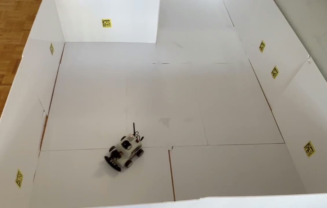The robot mid-run inside a white foam-board test arena, with yellow QR waypoint markers on the walls and floor.